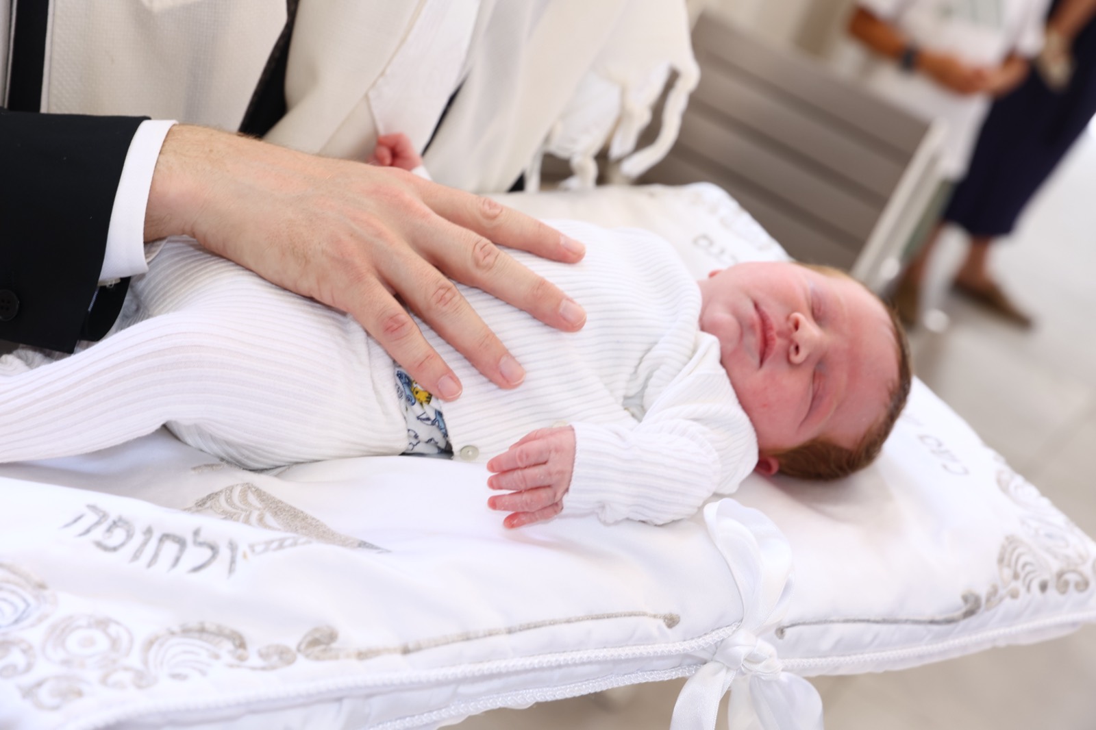 A newborn resting peacefully on an embroidered bris pillow